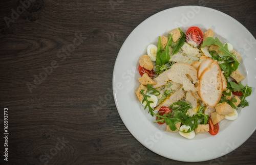 Caesar salad in a white plate on a wooden background
