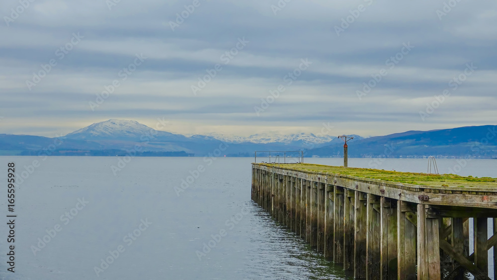 Derelict pier on the Firth of Clyde with snow covered mountains in distance