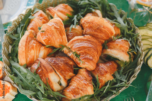 Appetizing croissants with meat and cheese filling and arugula in a woven rustic basket. Close up