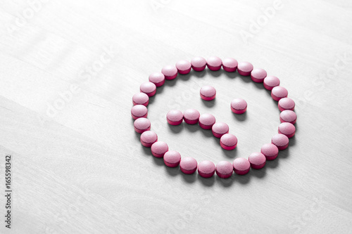 Clinical depression, mental illness and disorder or bad health services concept. Sad smiley face made from pills, medicine and tablets on wooden table. Dissatisfied and unhappy icon. photo