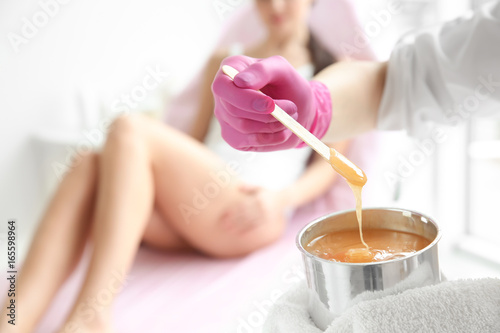 Female cosmetologist holding jar with wax for depilation on blurred background