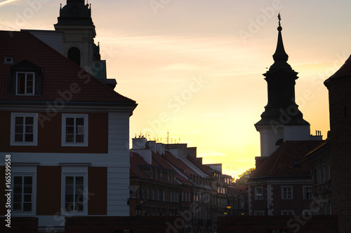 Sunset or sunrise in old town of Warsaw, Poland. Old buildings in dark shadow, almost silhouette. Beautiful yellow orange sky.