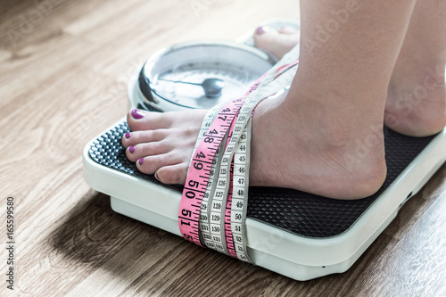 Anorexia and eating disorder concept. Feet tied up with measuring tape to a weight scale. Addiction and obsession to weight loss. photo