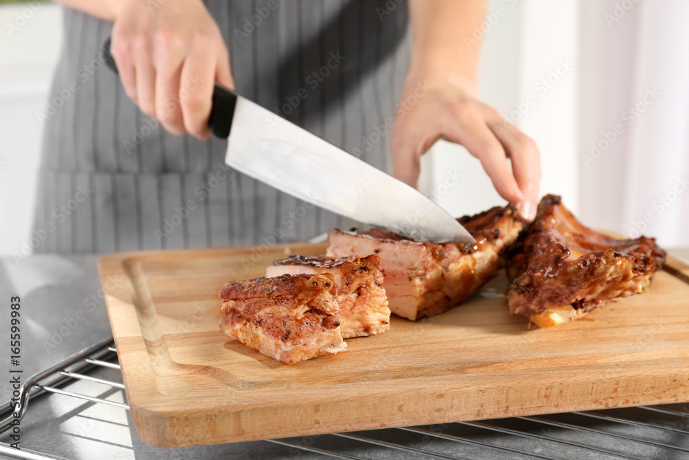 Woman cutting delicious pork ribs in kitchen, closeup