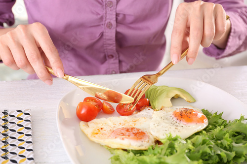 Fototapeta Naklejka Na Ścianę i Meble -  Woman eating tasty breakfast with fried eggs on white table