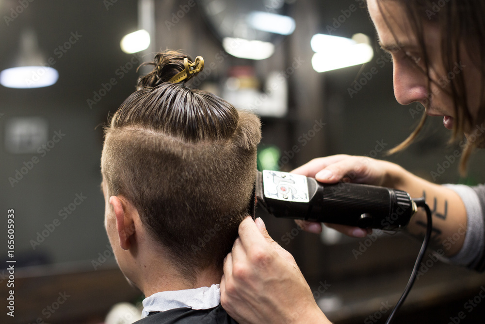 Barber in man hair salon gives trendy hipster millennial haircut, with shaved sides and manbun on top Stock Photo | Adobe Stock Barber in man hair salon gives trendy hipster millennial haircut, with shaved sides and manbun on top Stock Photo | Adobe Stock