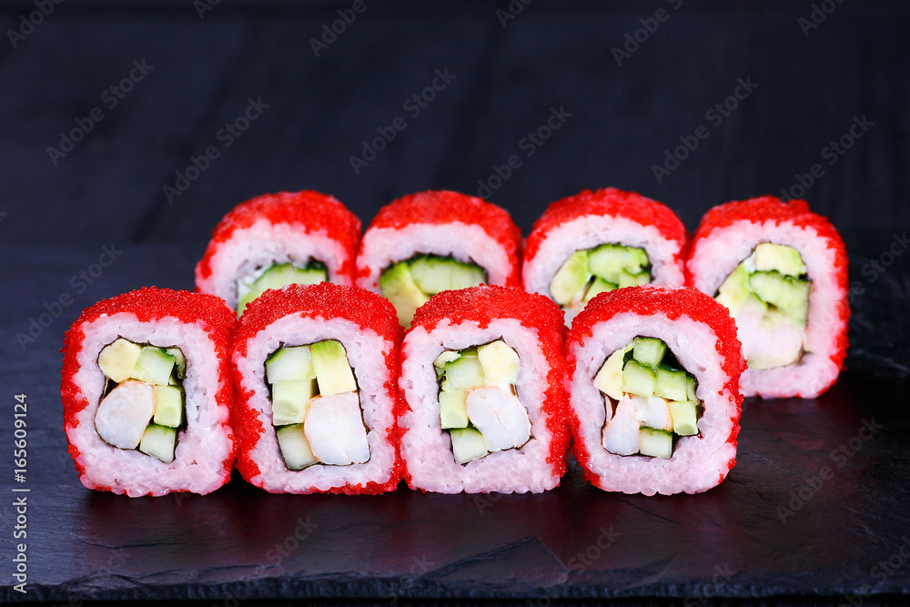 Delicious sushi roll with avocado, cucumber and cream cheese, covered with red caviar, served on black slate. Tasty japanese cuisine Delicious sushi roll with avocado, cucumber and cream cheese, covered with red caviar, served on black slate. Tasty japanese cuisine