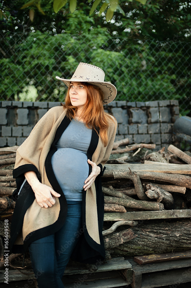 pregnant in cowboy wear sitting on wood at sunset