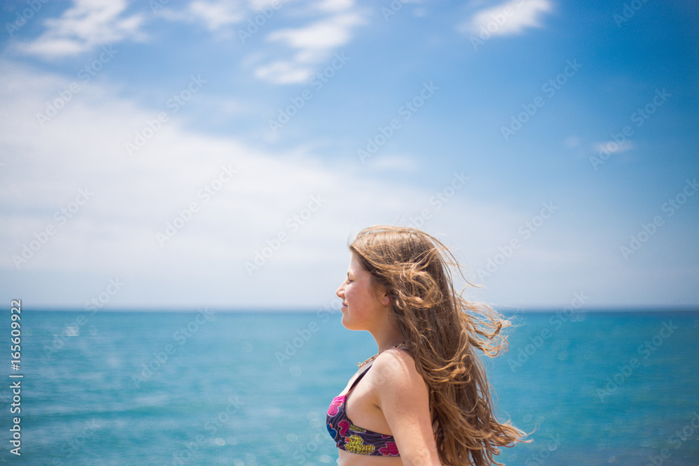 Naklejka premium A young blue girl stands out of arms, in the background of the sea, enjoys a holiday on the beach, and a sunburn