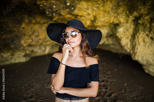Beautiful latin woman thinking  with hat and sunglasses sunbathing on rocks beach on summer vocation time © F8  \ Suport Ukraine