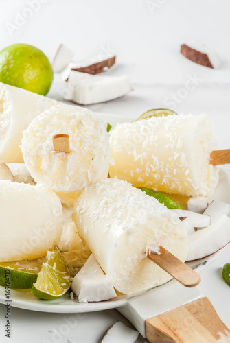 Summer desserts. Vegan diet food. Coconut and lime home fruit ice cream popsicles on a stick. On white marble table, copy space