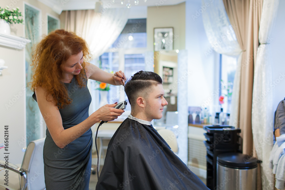Girl hairdresser with curly red hair cuts young, handsome guy in a beauty salon Girl hairdresser with curly red hair cuts young, handsome guy in a beauty salon
