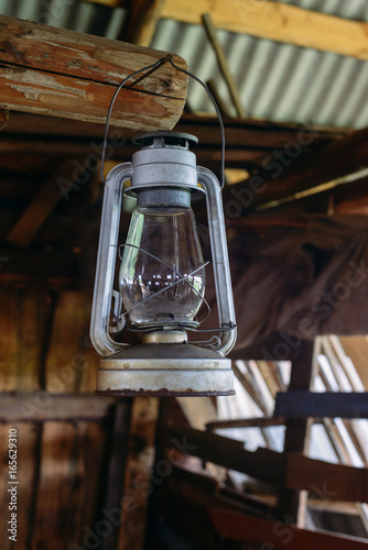 The old rusty kerosene lamp hangs on the nail in a half-ruined wooden building