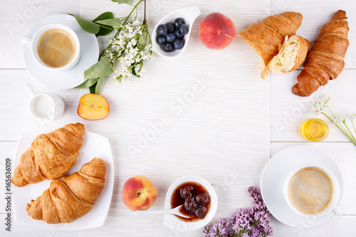 Breakfast - two cup of coffee, croissants, jam, honey and fruits on white table.