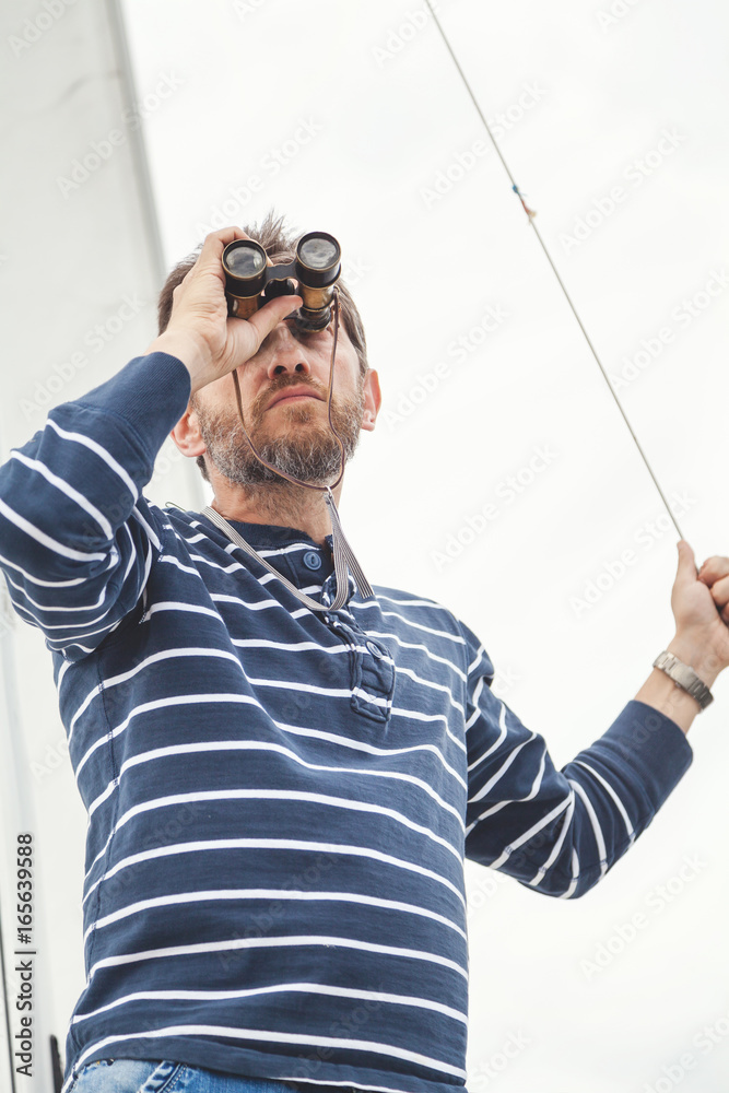 Naklejka premium man with beard looking through binoculars sailing yacht