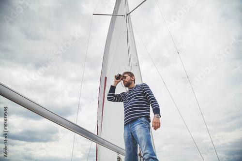 captain in striped shirt looking through binoculars sailing yacht