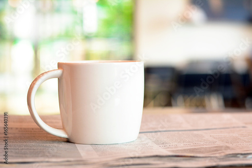 Coffee cup over newspaper on the table in blurred coffee shop background