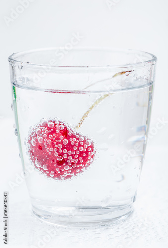 Ripe and sweet cherry in a glass of sparkling soda water placed on white background, healthy drinking concept.