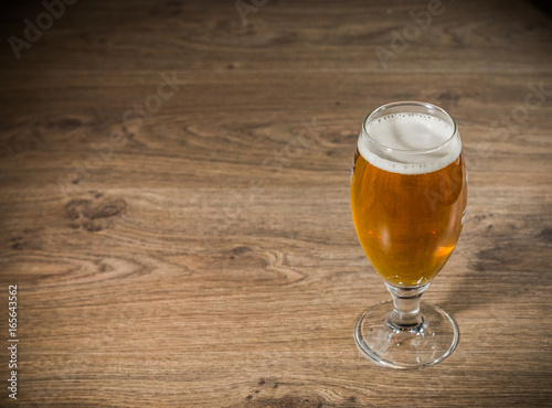A glass of beer with foam on a wooden background