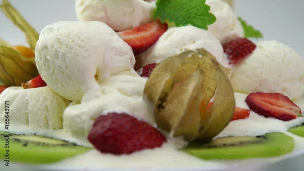 Ice cream dessert with fresh fruits, strawberries and mint leaves on a plate rotating against white background Ice cream dessert with fresh fruits, strawberries and mint leaves on a plate rotating against white background
