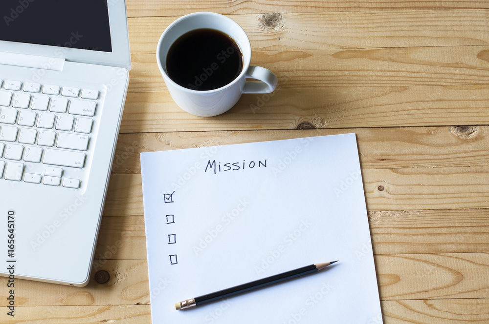 Paper check list for mission laptop and coffee on wood table.