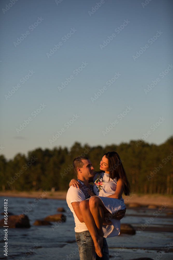 Fototapeta premium A young couple in love, on the shore of the Bay at sunset
