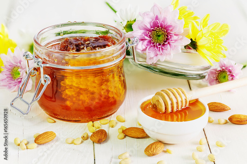 Honey with honeycomb in a glass jar on white boards, flowers, mendal, walnut
