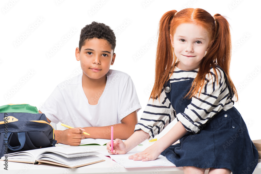 happy multiethnic schoolkids studying together and looking at camera isolated on white happy multiethnic schoolkids studying together and looking at camera isolated on white