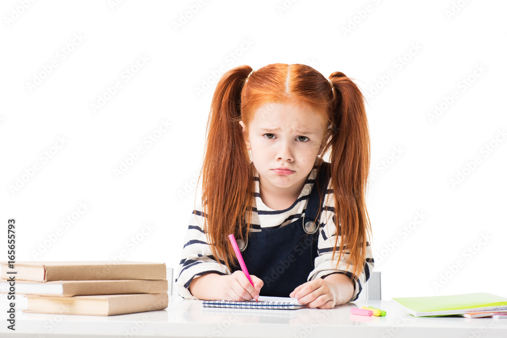 upset little schoolgirl drawing in notebook with felt tip pens and looking at camera isolated on white upset little schoolgirl drawing in notebook with felt tip pens and looking at camera isolated on white