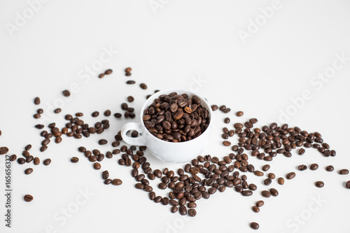 white cup with scattered coffee beans, isolated on white
