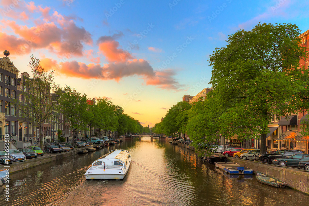 Tourist Canal tour boat at sunset in one of the beautiful canals of Amsterdam, The Netherlands
