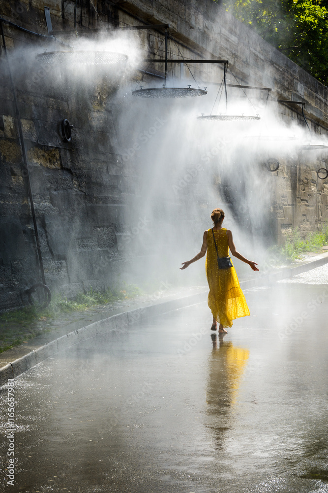 Φωτογραφία A woman is walking with her arms spread in the mist of a public water mister