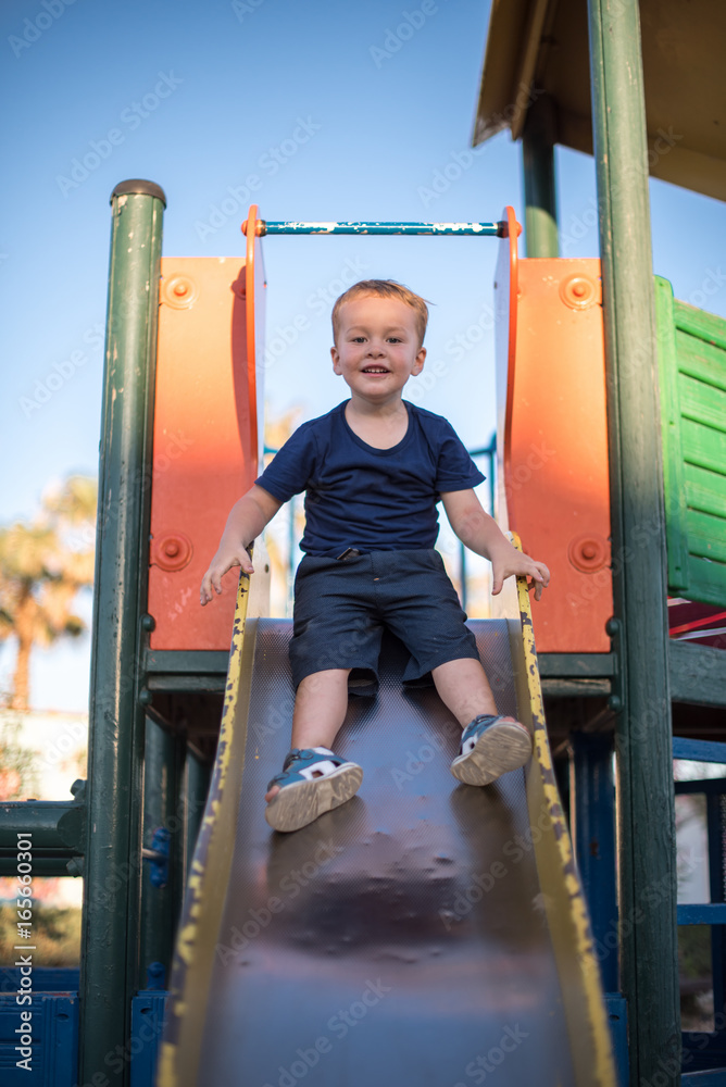 Fototapeta premium Happy boy riding from childrens slides