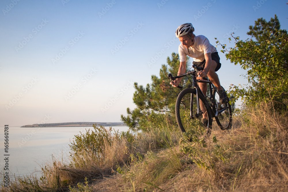 Fototapeta premium Bicycle rider on professional cyclocross bike ride downhill, pine and lake background 