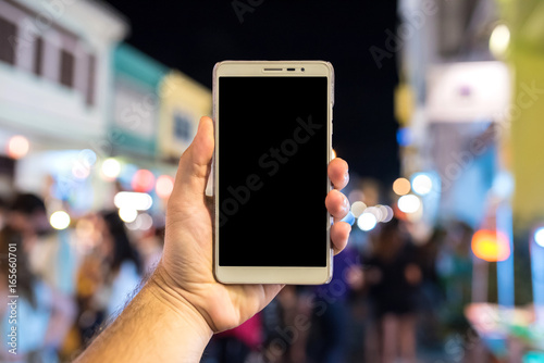 Man holding smart phone at a night market with lots of people.