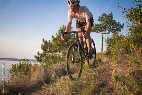 Bicycle rider on professional cyclocross bike ride downhill, pine and lake background 