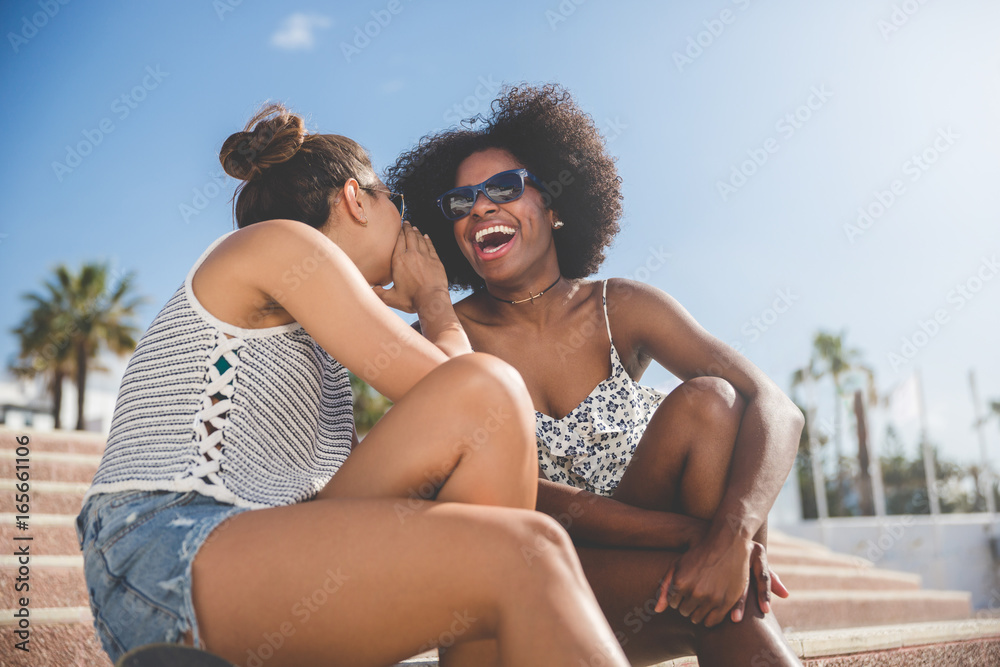 Young woman whispering to her laughing friend Young woman whispering to her laughing friend