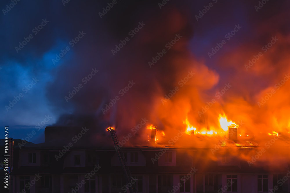 Building in fire, burning fire flame with smoke on the apartment house roof at night in the city