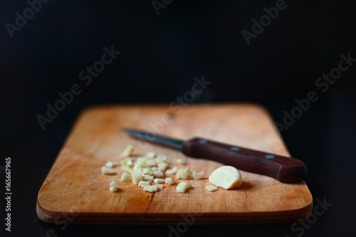 Selective focus image of chopped garlic and a knife on a wooden board.