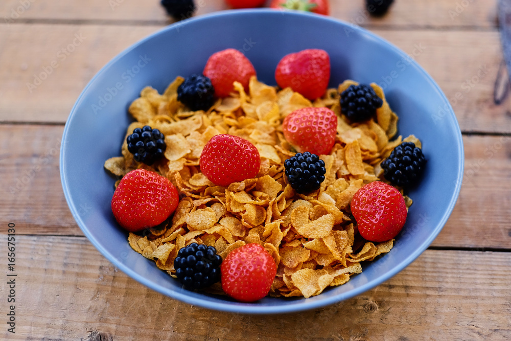 Corn flakes on a strawberry and blackberry on a plate.