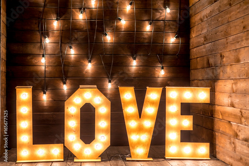 Luminous letters love.Volumetric letters on a wooden background with a garland of incandescent lamps