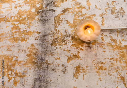 Incandescent light bulb on old wall - A bright lit incandescent light bulb with yellow filament on an old chipped wall.