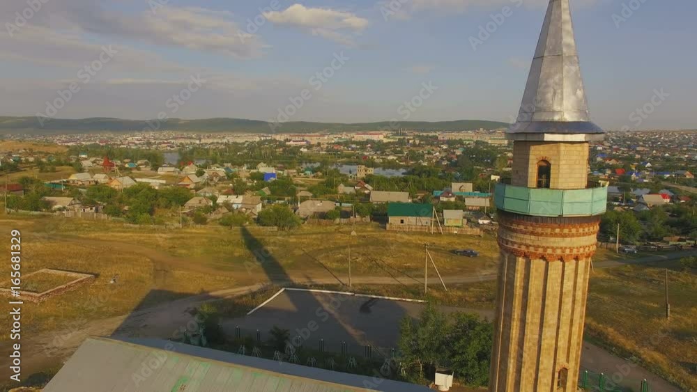 AERIAL: View from above on old mosque in mountain countryside. White clouds, green grass and sunny sunrise. Beautiful hills and blue sky in perspective, behind the rural town. AERIAL: View from above on old mosque in mountain countryside. White clouds, green grass and sunny sunrise. Beautiful hills and blue sky in perspective, behind the rural town.