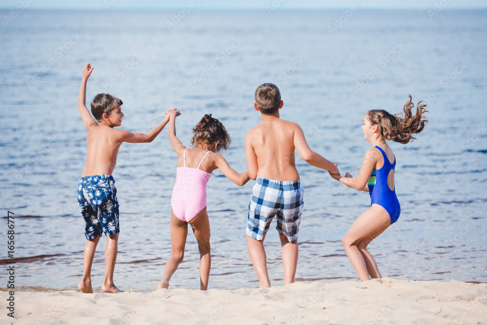 rear view of group of little children holding hands while standing on sandy beach
