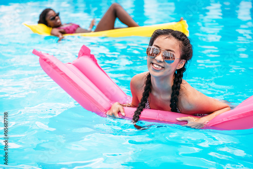 Young multiethnic women floating on inflatable mattresses in swimming pool at resort