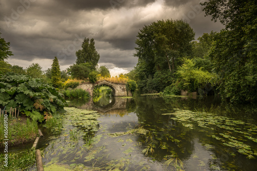 English historic medieval bridge overlooking river Avon beside Warwick Castle with lush green foliage and wild summer storm clouds. photo