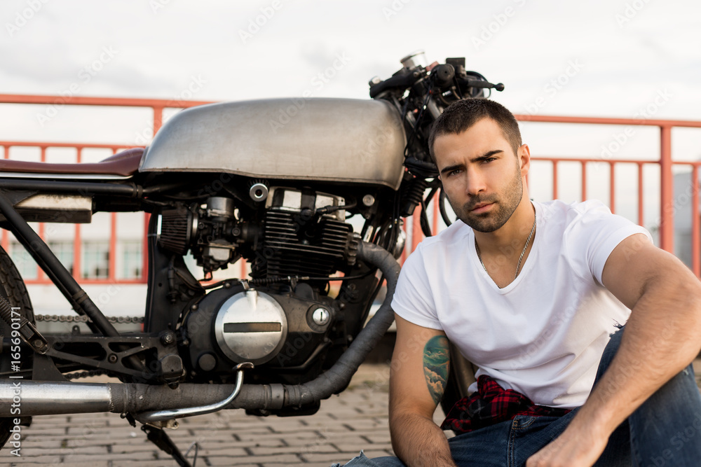 Φωτογραφία Handsome happy rider man with beard and mustache sit near his classic style biker cafe racer motorcycle and look to the camera