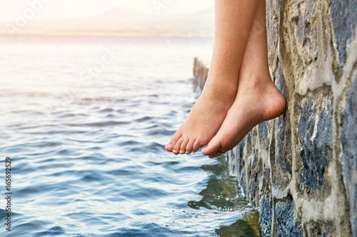  Wet bare girl's feet dangling from the jetty 