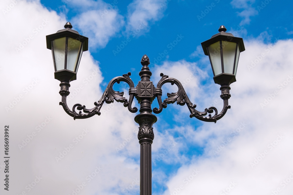 Two lamps on a forged metal lantern in retro style on a background of sky