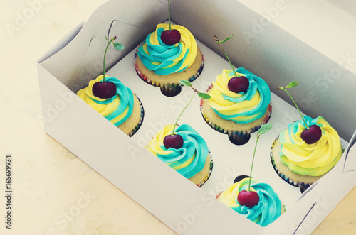 Vanilla cupcakes with a cap of cream on light wooden tablein the box photo